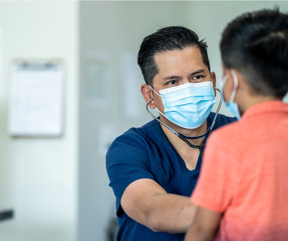 Masked medical professional listening to boy's chest